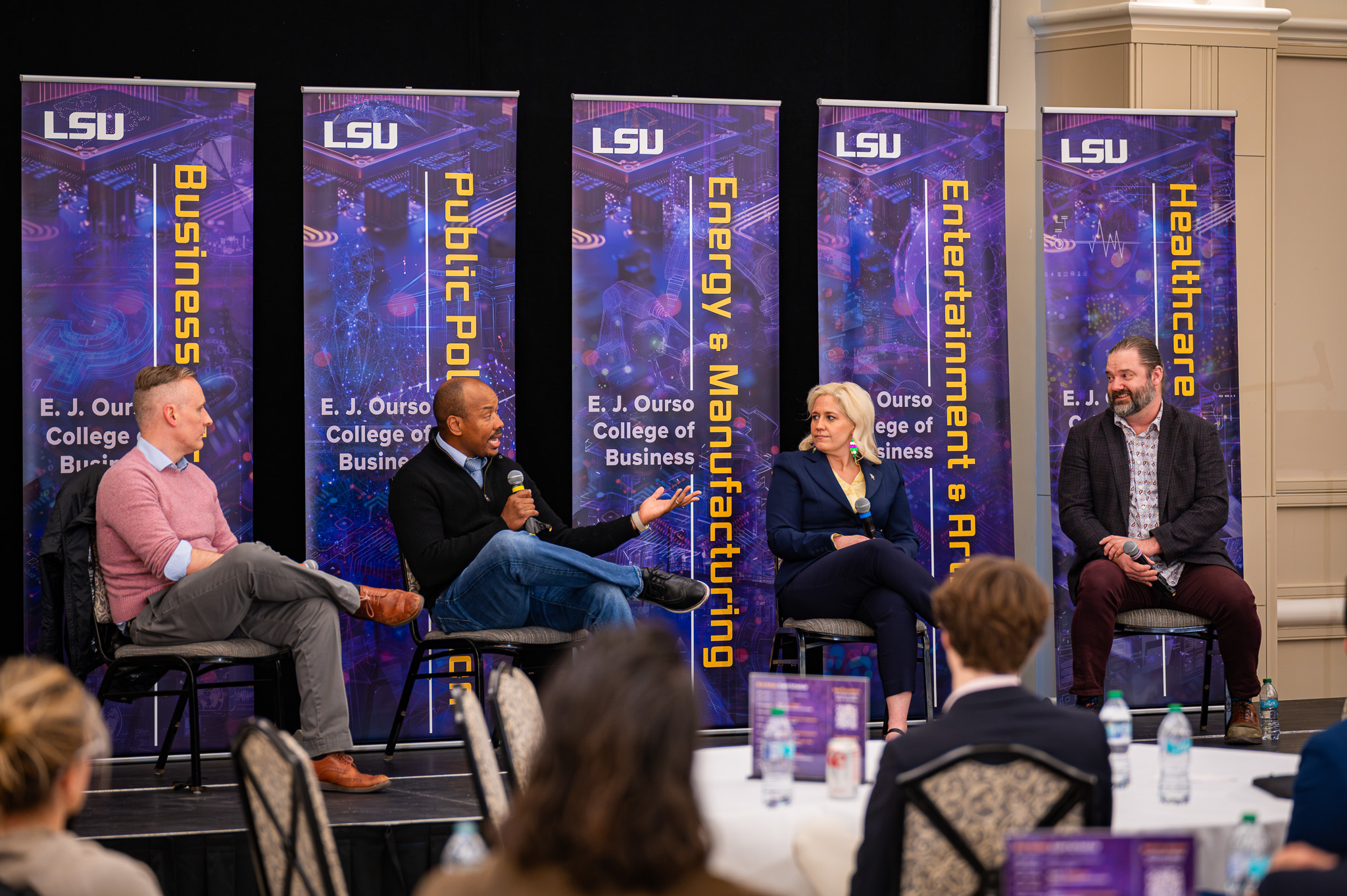 Panel of four people sit in chairs on a stage