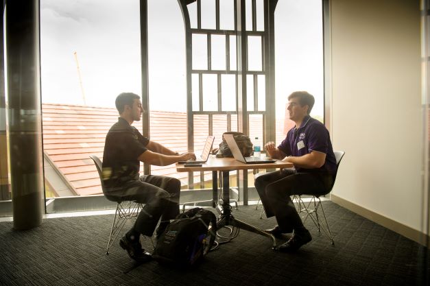 Two students talk at table in BEC rotunda